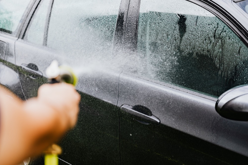 Black sedan being carefully rinsed during an exterior detail