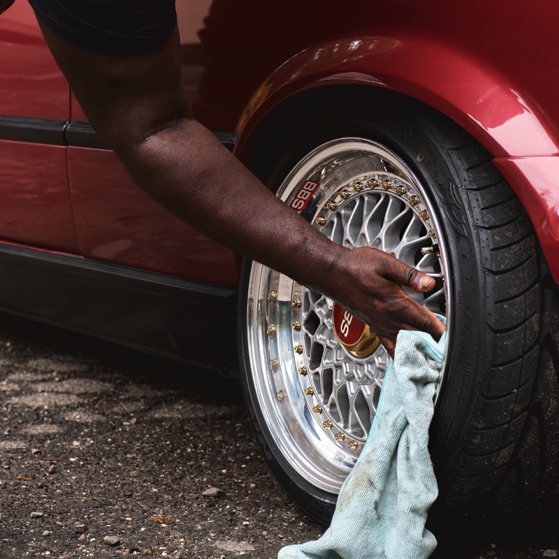 Detailer wiping a polished wheel on a red vehicle